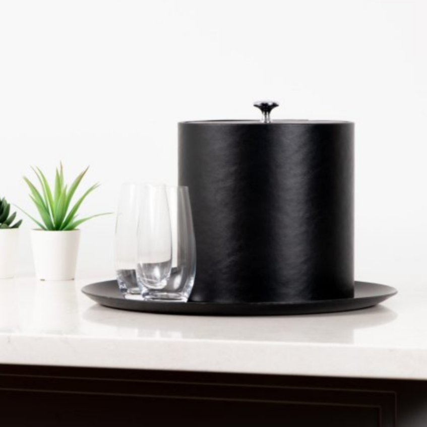 Black ice bucket on a white surface with plants and glasses in the background