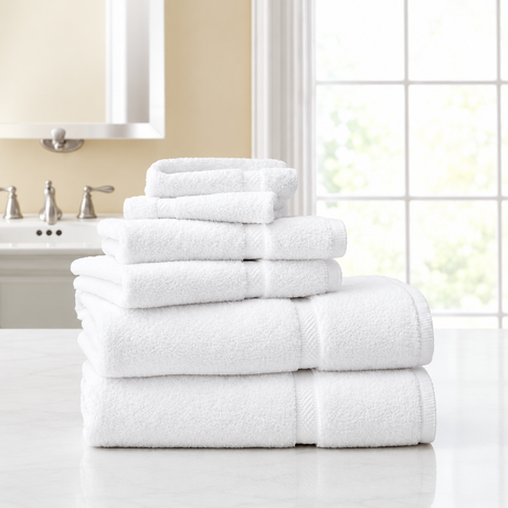 Pictured: Stack of white towels on a white counter in a clean bathroom. The towels are neatly folded and stacked from largest to smallest