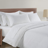 White bedding set on a wooden bed with a lamp in the background