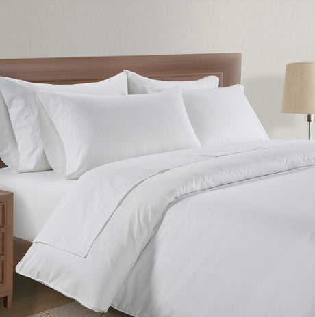 White bedding set on a wooden bed with a lamp in the background