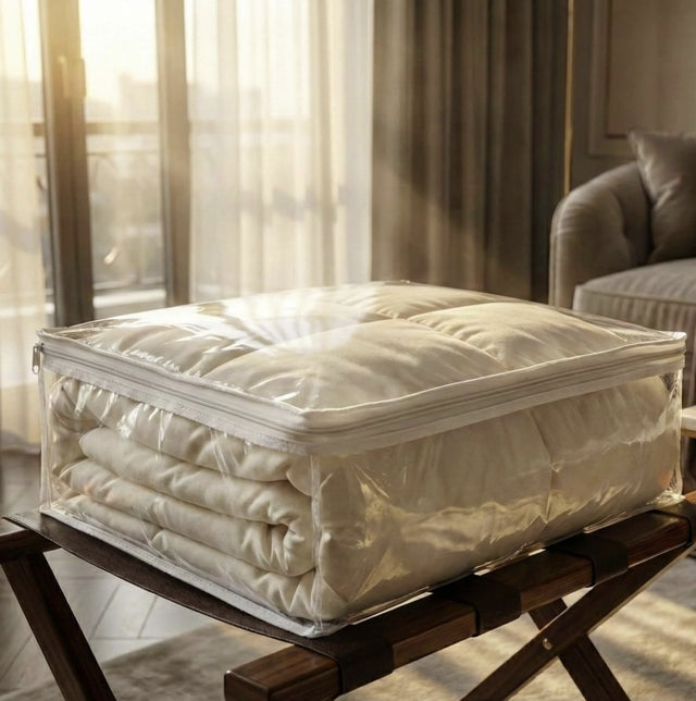 Stack of folded bedding in a clear storage box on a wooden table with a blurred indoor background