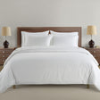White bedding set on a bed with wooden headboard and nightstands with lamps.