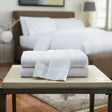 Stack of white towels on a wooden table with a blurred bedroom background