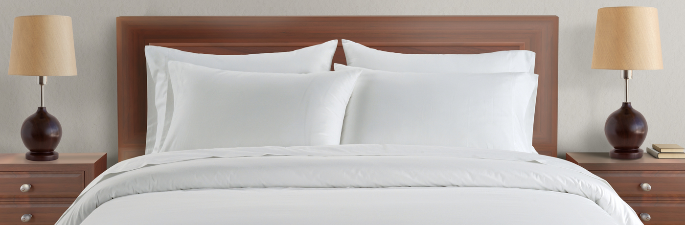 White bedding set on a bed with wooden headboard and lamps on either side.