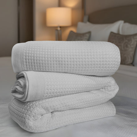 Stack of gray textured blankets on a bed with a blurred bedroom background