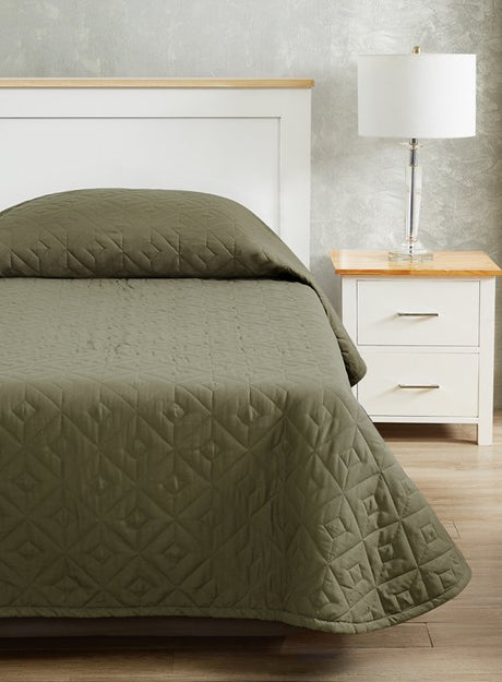 Pictured: Nicely made bed on a white wooden bed frame with a matching nightstand  and lamp to the right. The bed features the CozyCare DESIGNS Bedspread in the shade "Moss".