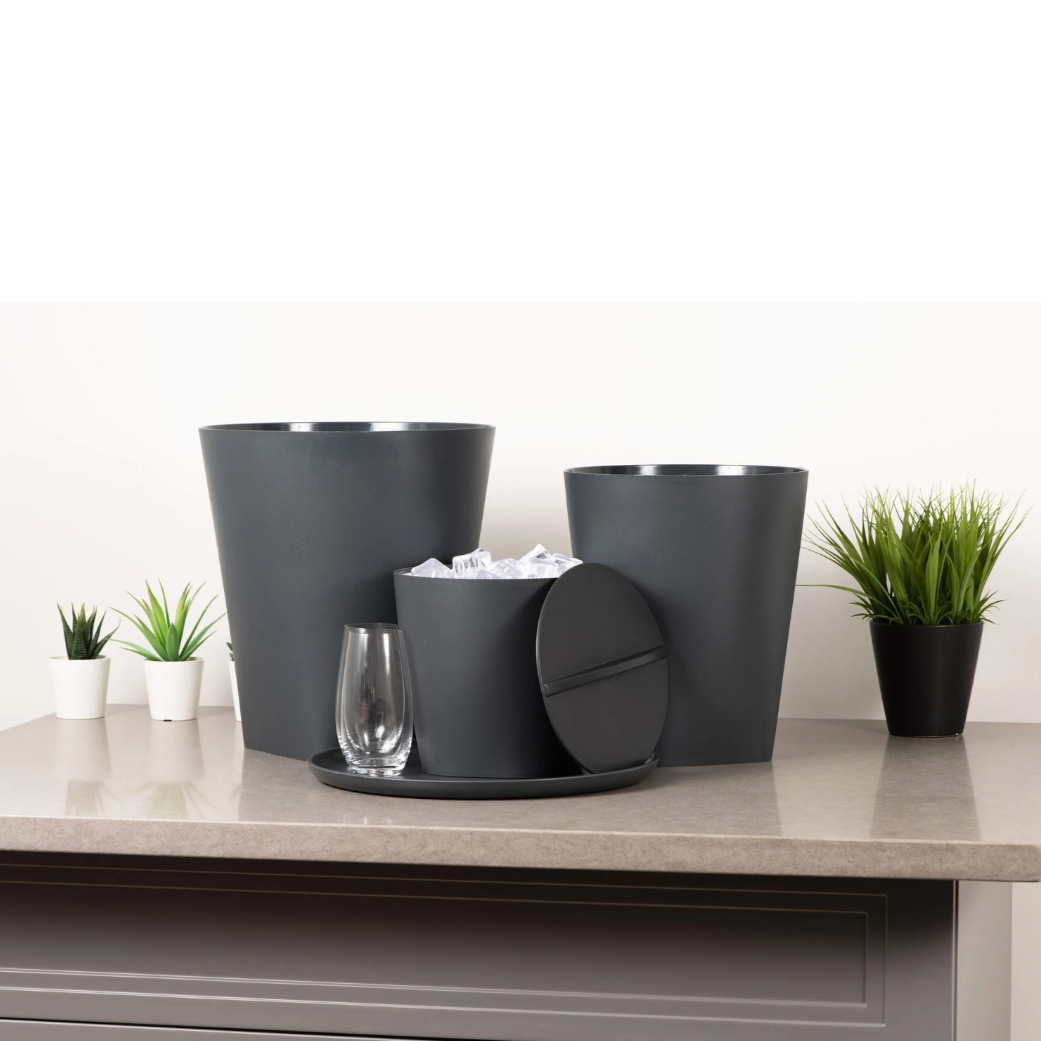 Set of dark gray planters and a glass on a light-colored surface with a white background