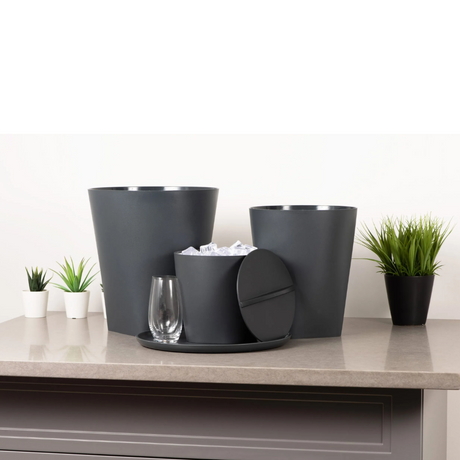 Set of dark gray planters and a glass on a light-colored surface with a white background