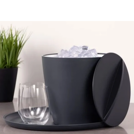 Dark gray ice bucket with lid, glass of water, and ice cubes on a light surface.
