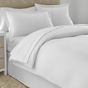 White bedding set on a bed with beige headboard and carpet.
