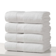Pictured: Four neatly folded white towels stacked on top of each other on a counter against a white background. 