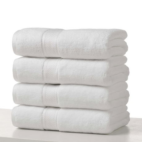 Pictured: Four neatly folded white towels stacked on top of each other on a counter against a white background. 