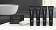 Pictured: Infuse Amenity collection lined up on a white marble counter with a bathtub in the background. Products pictured from left to right are: Infuse Cleansing Bar, Infuse Shampoo, Infuse Conditioner, Infuse Body Wash and Infuse Lotion. All products made with lavender mint. The cleansing bar comes in a black cardboard box with gold accents. Every other product pictured comes in a black squeeze tube with gold accents and a flip cap.