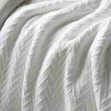 A close-up of a white textured throw blanket with a cable-knit pattern, draped in soft folds.