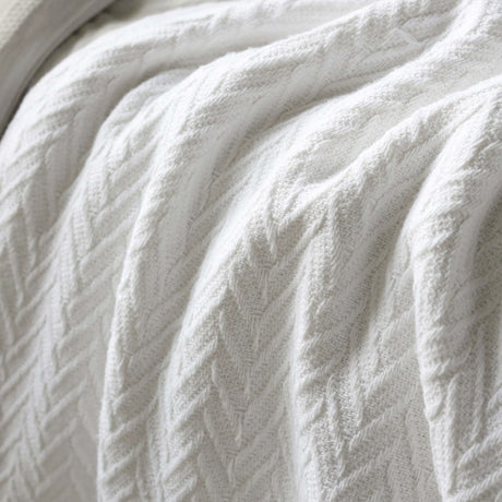 A close-up of a white textured throw blanket with a cable-knit pattern, draped in soft folds.