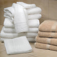 Pictured: Neatly folded stack of the Magnificence Towel collection against bathroom tile. The collection comes in the shades White (left) and Linen (right).