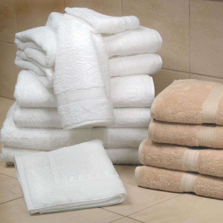 Pictured: Neatly folded stack of the Magnificence Towel collection against bathroom tile. The collection comes in the shades White (left) and Linen (right).
