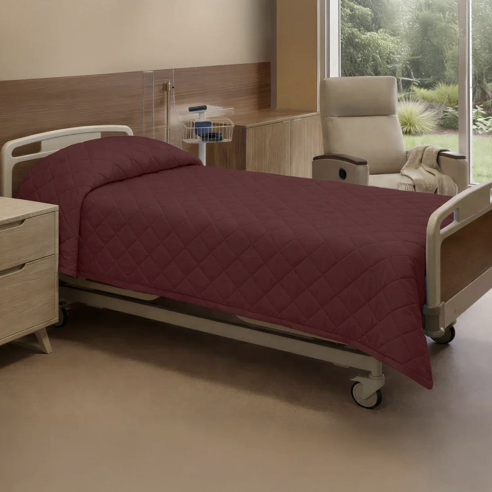 Hospital bed with maroon quilt in a room with a chair and window