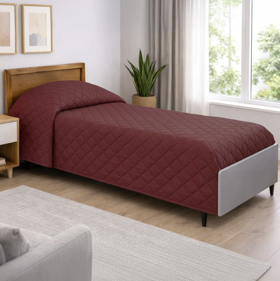 Bed with a red quilt in a room with a window, plant, and furniture.