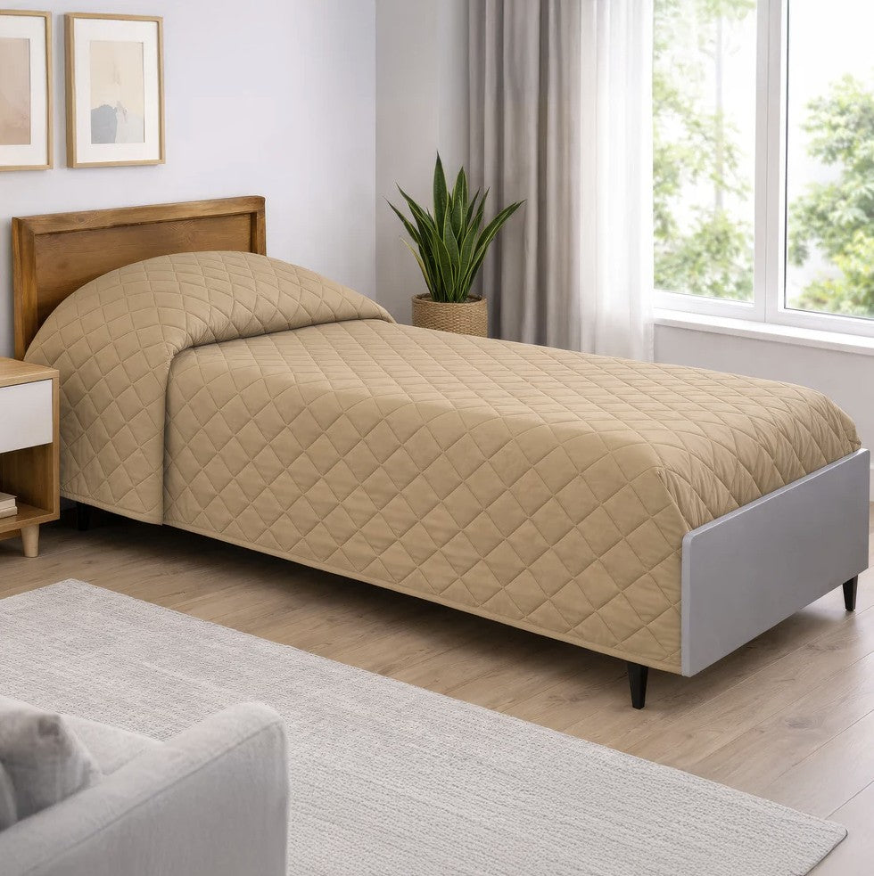 Beige quilted bedspread on a bed in a bright bedroom with a window and plant.