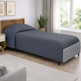 Bed with a blue quilt in a bedroom setting with a window and plant.
