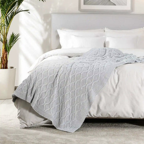 Gray textured blanket draped over a bed in a bedroom setting with a plant and framed picture.