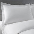 Pictured: Closeup of a pillow on a nicely made white bed against a grey headboard. The pillow is wearing he Millennium T-250 Pillow sham in the Solid White style.