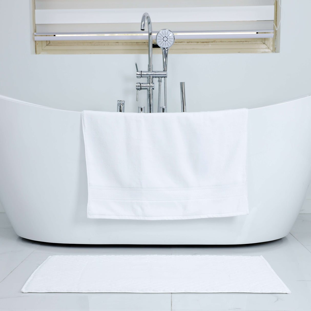 White freestanding bathtub in a modern bathroom with a towel draped over it.