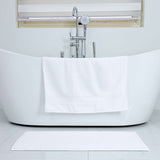 White freestanding bathtub in a modern bathroom with a towel draped over it.