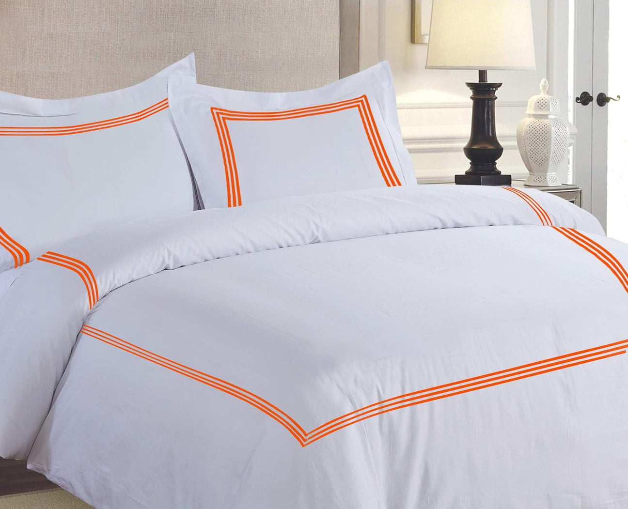 White bedding set with orange trim on a bed in a bedroom setting.