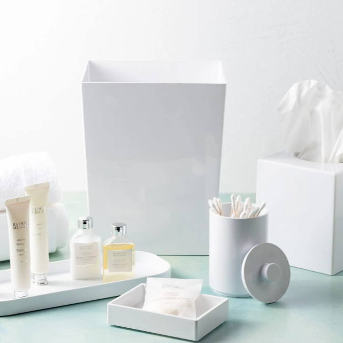 White bathroom accessories including a soap dish, toothbrush holder, and tissue box on a light blue surface.