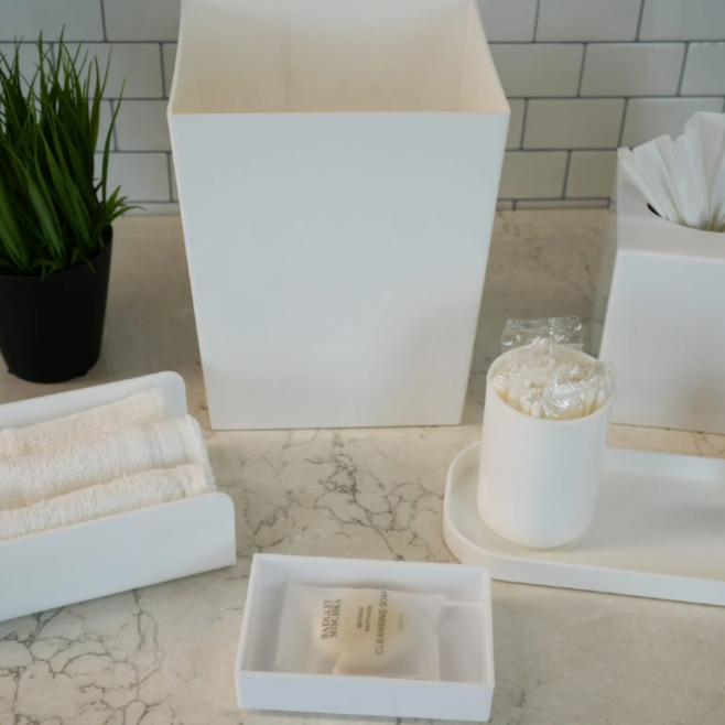 White bathroom accessories including a square vase, tissue box, and other items on a marble countertop.
