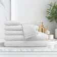 Stack of white textured towels on a white surface with decorative items in the background