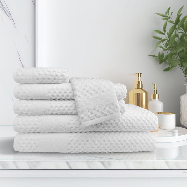 Stack of white textured towels on a white surface with decorative items in the background