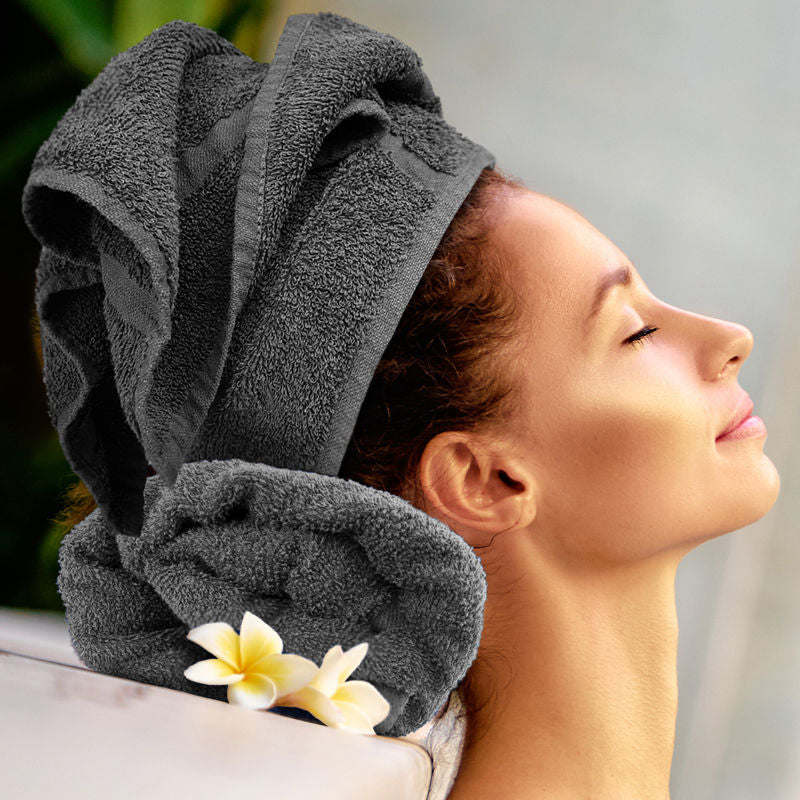 Woman with a gray towel wrapped around her head, eyes closed, with a blurred background