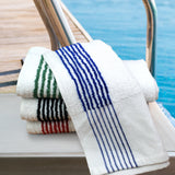 Stack of towels with striped patterns on a boat railing by a pool.