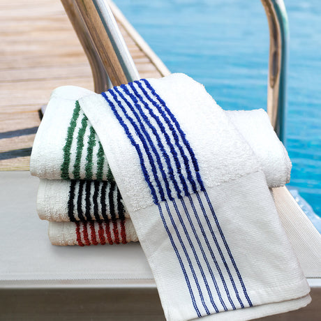 Stack of towels with striped patterns on a boat railing by a pool.