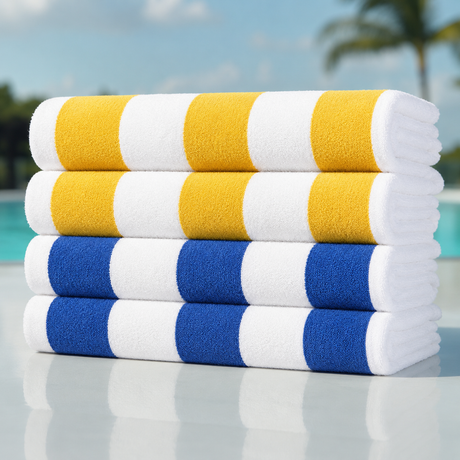Four stacks of striped beach towels rolled up, featuring yellow and white, and blue and white patterns, set against a blurred background of a swimming pool and palm tree.