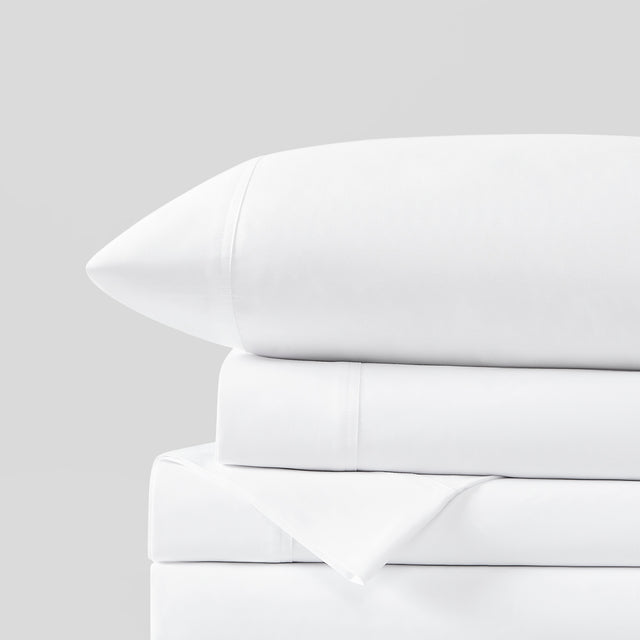 Stacked white bed sheets and pillowcase on a gray background
