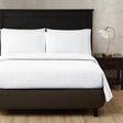 Pictured: Bedroom setting with a dark fabric bed frame holding a nicely made white bed with a dark wood nightstand to the right. A silver lamp sits atop of the nightstand. The top sheet pictured has a waffle texture/pattern.