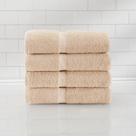 A stack of five folded beige cotton towels with ribbed bands, displayed on a glossy white surface against a white subway tile wall.