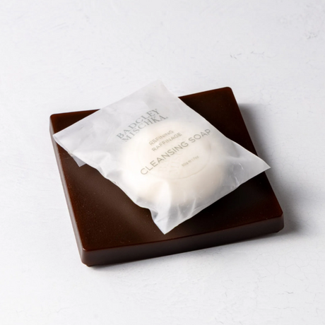 White soap bar in a clear plastic bag on a brown square soap dish with 'Bourjois' branding.