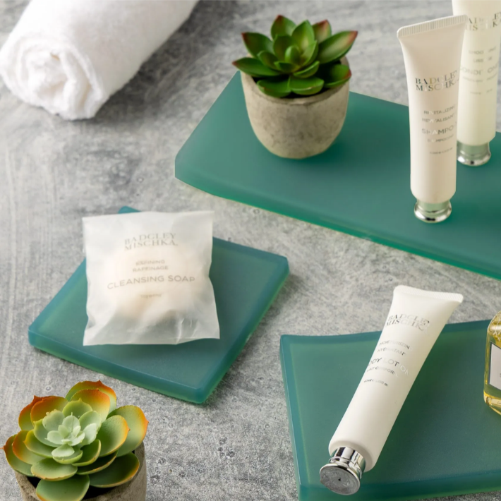 Cosmetic products on green trays with succulents on a gray surface