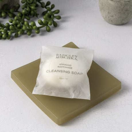 Cleansing soap bar with a white label on a light surface, accompanied by greenery.