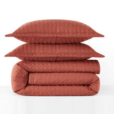 Folded quilt and pillows in a terracotta color on a white background