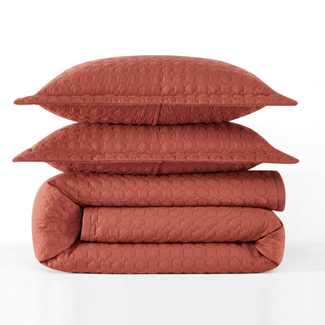 Folded quilt and pillows in a terracotta color on a white background