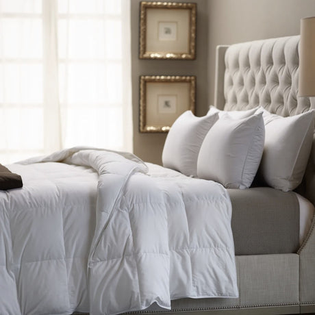 Neatly made bed with white bedding and gray headboard in a bedroom setting.