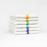 Pictured: Six white bar mops with a colored stripe down the middle neatly folded and stacked against a white background. There are two of each colored stripe. From top to bottom the colors are: Gold, Green and Blue.