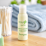 Pictured: Small standing clear bottle  holding cream with a clear cap in the forefront of a bathroom setting. The bottle is part of a spa line called Nourish, this product is the vitamin enriched body lotion with lemongrass. The bottle holds 1 fluid oz. (30 mL)
