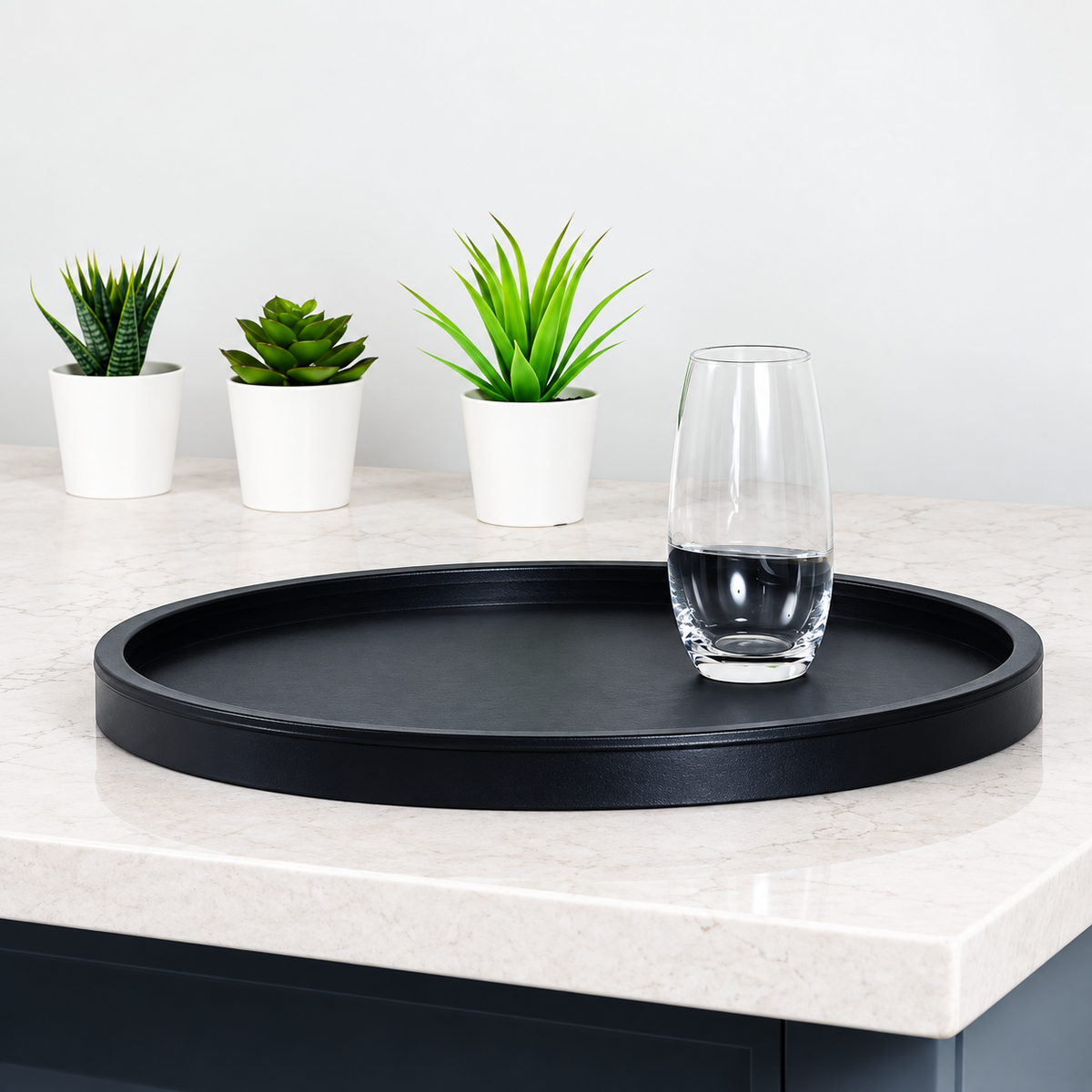Pictured: A countertop holding 3 small potted plants and a glass on a black leatherette tray.